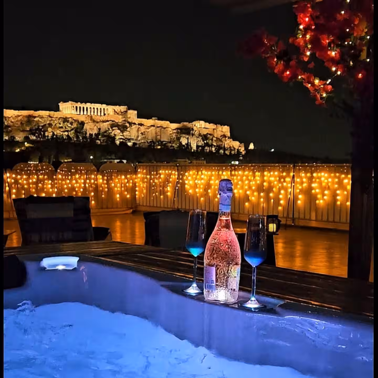 Rooftop jacuzzi at night with wine and the illuminated Acropolis in the background
