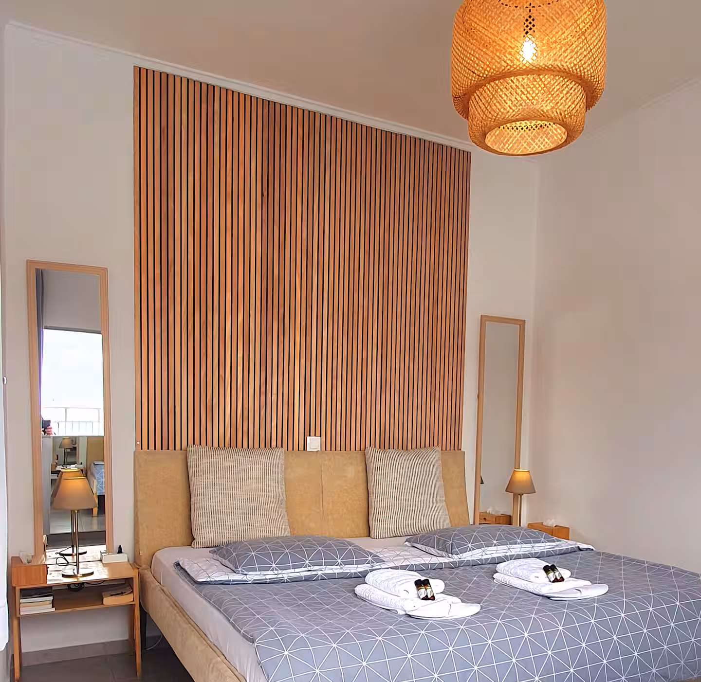 Bedroom with wood-slat headboard, rattan pendant light, and freshly made bed