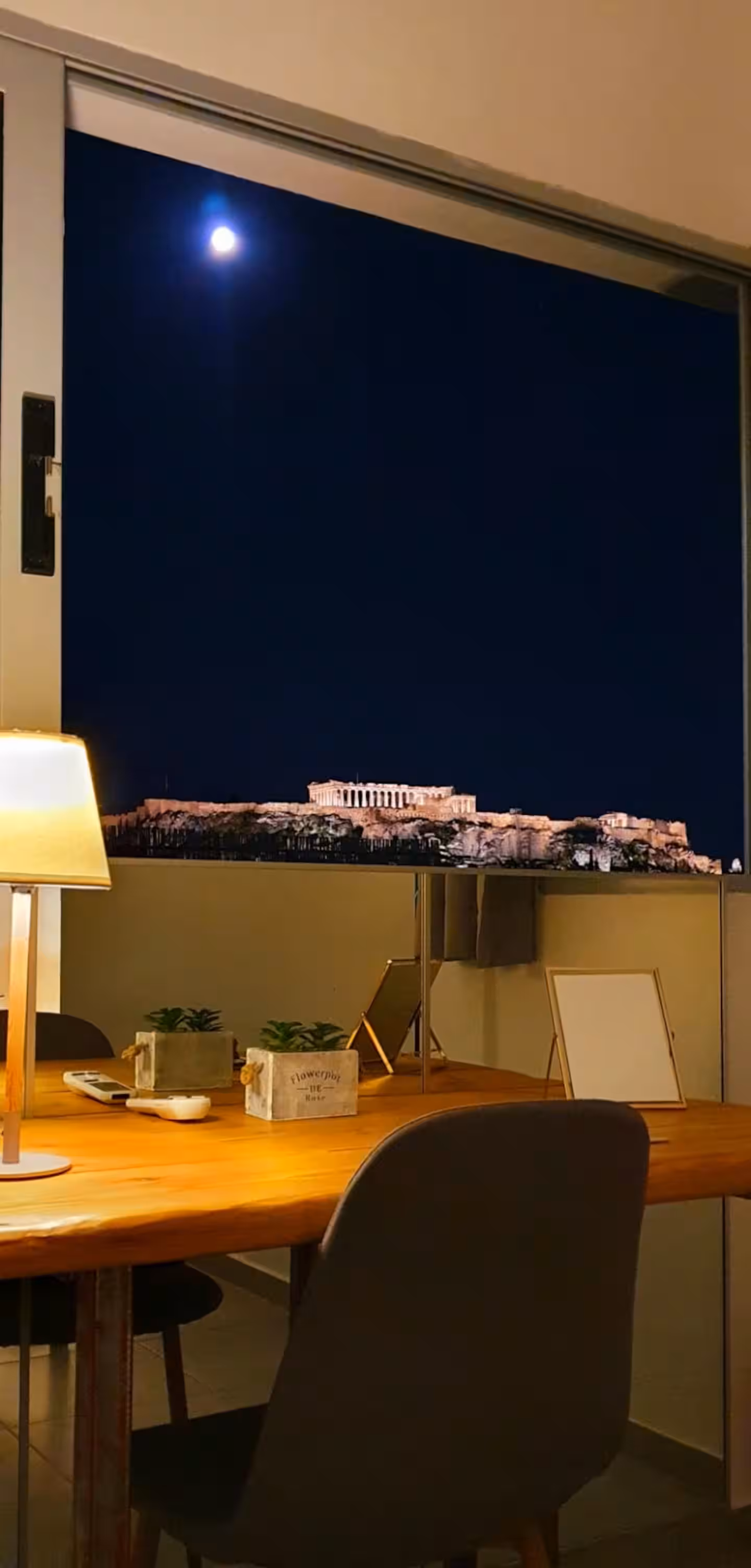 Night view of the moonlit Acropolis framed by the apartment window
